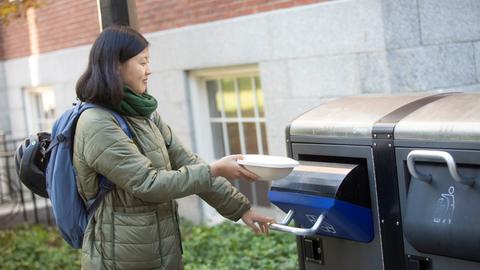 Someone opening an exterior recycling bin and placing an item inside
