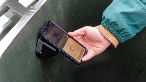 Someone holding a phone scanning a sensor in a waste bin