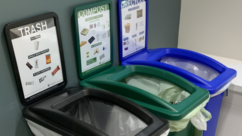 A trash bin, a recycling bin, and a compost bin placed next to each other. 