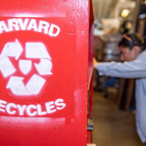A side view of a bookshelf that says "Harvard Recycles" with someone browsing the shelves
