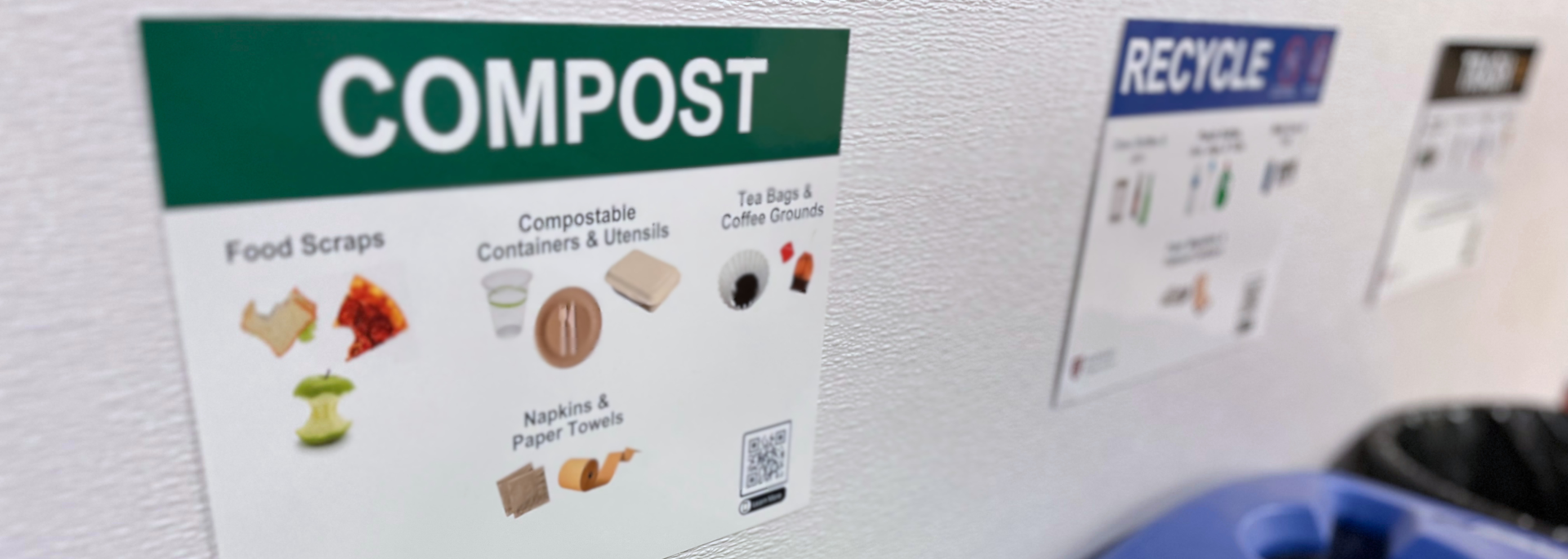 Compost signage and bin, next to a labeled recycling bin and trash bin