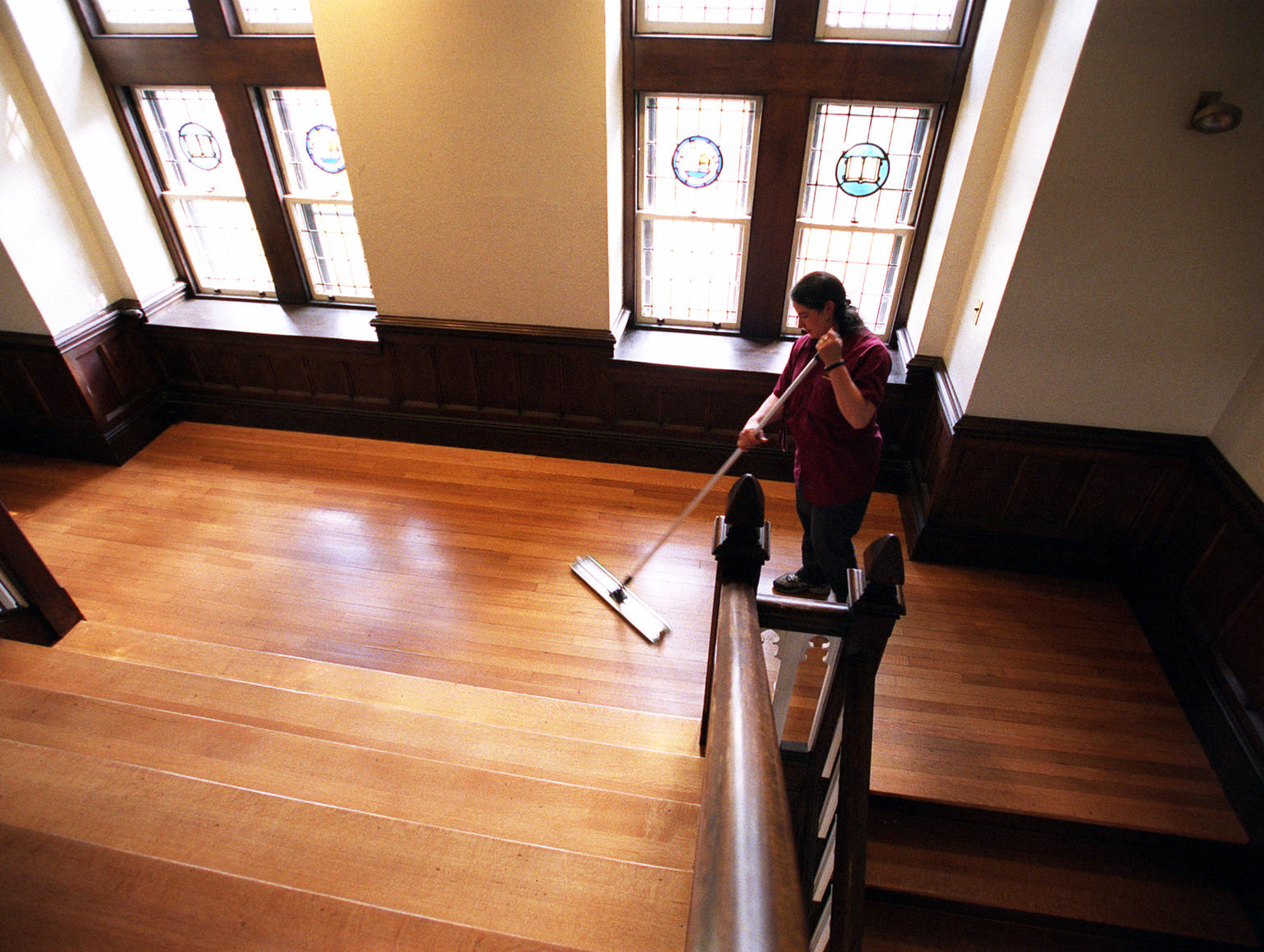 Custodian mops gleaming wood floor as sun pours through stained glass windows