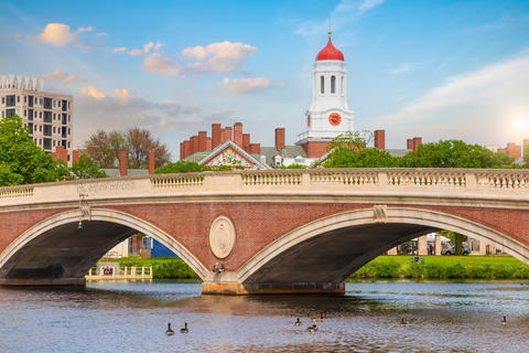 A brick footbridge over a river, with campus buildings in the background